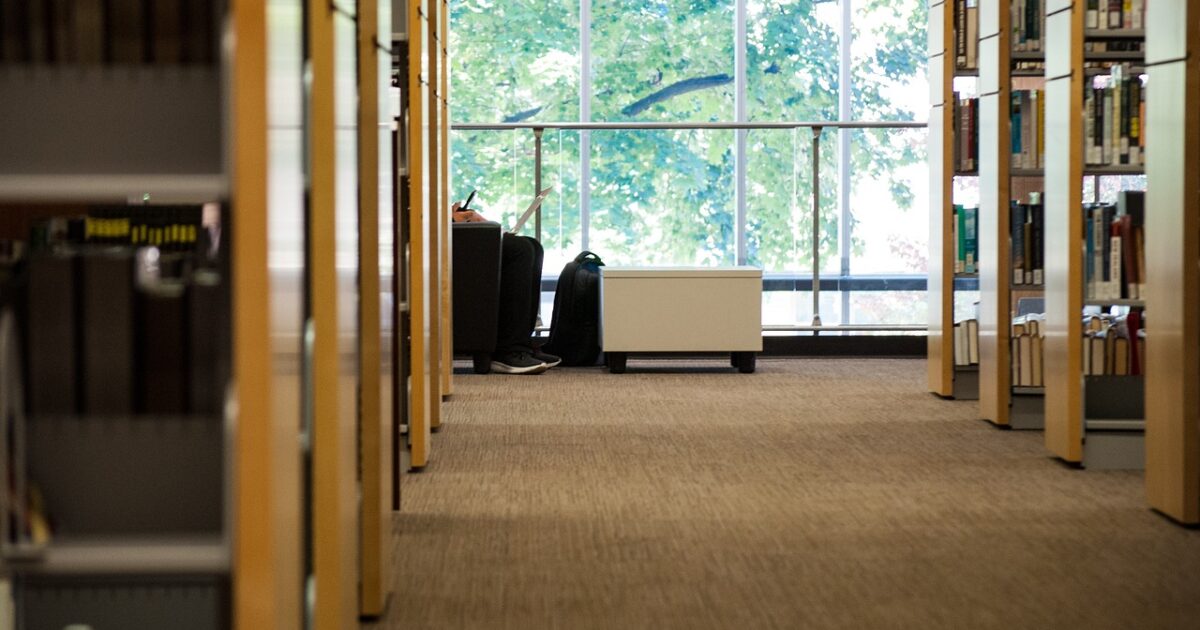 図書館の書架と窓際でノートパソコンを使う人物