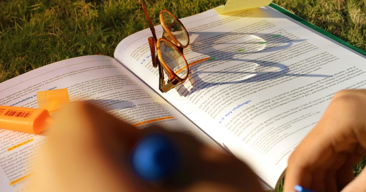 屋外の芝生で教科書にマーカーを引きながら勉強する様子